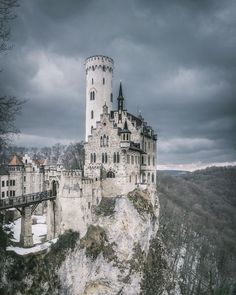 a castle on top of a cliff with a bridge in the foreground and dark clouds overhead