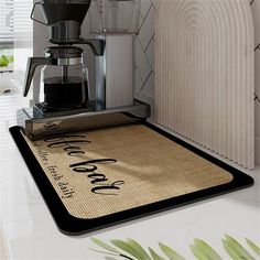 a coffee maker sitting on top of a counter next to a mat with the words you're here