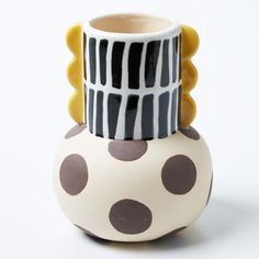 a white and black vase with polka dots on it's sides, sitting in front of a white background