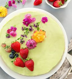 a cake decorated with flowers and strawberries on a white plate next to two bowls of fruit