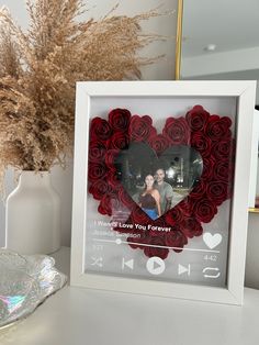 a white frame with a red rose heart in the shape of a photo and a vase full of dried flowers