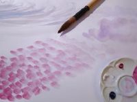 a paintbrush and palette on a white surface with pink watercolors in the background