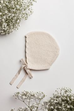 a knitted bonnet sits next to some baby's breath flowers on a white surface