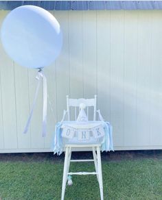 a baby's first birthday chair with a blue balloon attached to it, sitting in front of a white wall