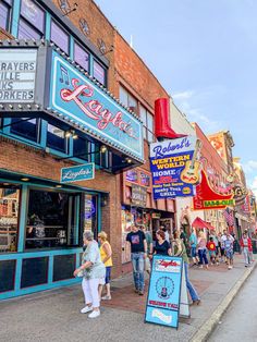 people are walking on the sidewalk in front of shops and stores that have neon signs