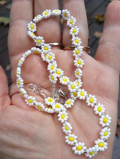 a hand holding a white and yellow beaded bracelet with flowers on the clasps