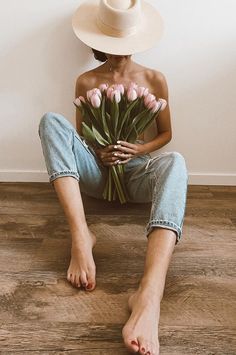 a woman sitting on the floor with her legs crossed holding a bouquet of pink tulips