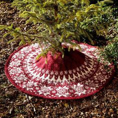 a red and white crocheted hat sitting on the ground next to a tree