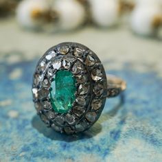 This antique Georgian ring features a .72 carat emerald and accent diamonds in two-tone 14 karat yellow gold and sterling silver. The oval cut emerald has a green-blue hue and is prong set in the center of an oval mounting. Thirty (30) accent diamonds halo the center emerald with six (6) accent diamonds decorating the shoulders of the band, set in sterling silver. From the profile, an openwork basket mounting holds the collection of gemstones finished on a polished and engraved 14 karat yellow g Georgian Ring, Marquise Diamond Engagement Ring, Diamond Cocktail Rings, Eternity Ring Diamond, Art Deco Diamond, Shop Engagement Rings, Emerald Ring, Lab Created Diamonds, Halo Diamond