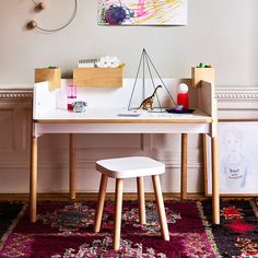 a desk and chair in front of a painting on the wall, with artwork above it