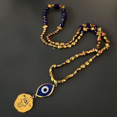 Good Luck Evil Eye and Hamsa Necklace, is a stunning fusion of cultural symbolism and elegant design. This captivating necklace is meticulously crafted, featuring a combination of gold-colored hematite stone beads, blue crystal beads, a sterling silver Hamsa pendant plated with 18k gold, and an 18k gold-plated evil eye glass pendant. At the heart of the necklace lies a sterling silver Hamsa pendant, plated with 18k gold. The Hamsa symbolizes protection and blessings in many cultures, serving as Hand-strung Beaded Necklaces As Festival Gifts, Festive Hand-strung Beaded Necklaces As Gifts, Artisan Handmade Temple Necklace As Gift, Spiritual Gold Crystal Necklace, Festive Gemstone Beads Spiritual Jewelry, Symbolic Gemstone Bead Necklaces For Gifts, Spiritual Beaded Necklaces With Polished Beads For Festivals, Spiritual Style Polished Beaded Necklaces For Festivals, Gold Adjustable Amulet Beaded Necklaces