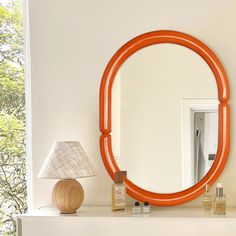 an orange round mirror on top of a white mantle