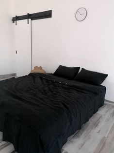 a bed with black sheets and pillows in a white room next to a clock on the wall