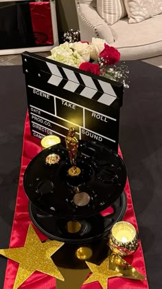 a table topped with a movie clapper next to a vase filled with flowers and candles