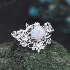 an opal and diamond ring sitting on top of a rock