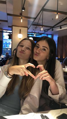 two young women sitting at a table making a heart shape with their hands in front of them