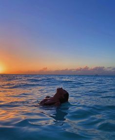 a man laying on his back in the ocean at sunset