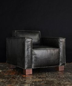 a black leather chair sitting on top of a wooden floor in front of a black wall