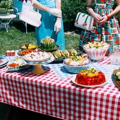 two women standing in front of a table full of food on plates and bowls,