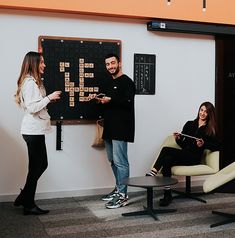 two people standing in front of a board with scrabbles on it and one person holding a tablet