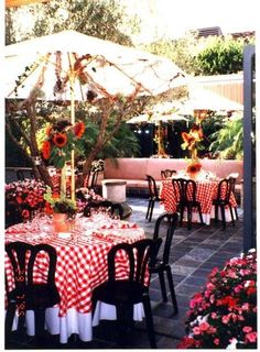 an outdoor dining area with red and white checkered tablecloths, sunflowers, and umbrella