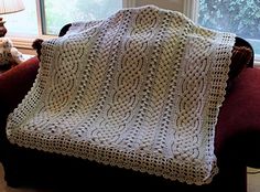 a white crocheted blanket sitting on top of a couch next to a window