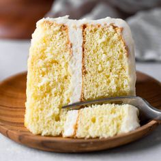 a slice of white cake on a plate with a fork next to it and the rest of the cake in the background