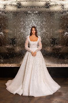 a woman standing in front of a fountain wearing a white wedding dress with long sleeves