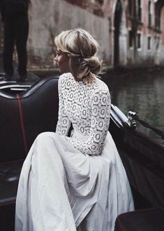 a woman sitting in a gondola on the side of a river wearing a white dress