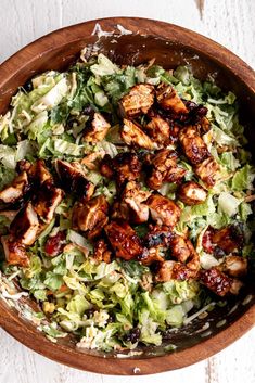 a salad with chicken and lettuce in a wooden bowl on a white table