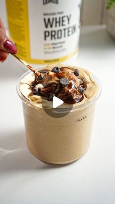 a person is holding a spoon over a cup of ice cream with chocolate chips on top