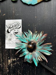 a flower brooch sitting on top of a wooden table next to a piece of paper