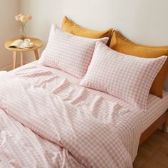 a pink and white checkered comforter set on a bed with two pillows in the corner