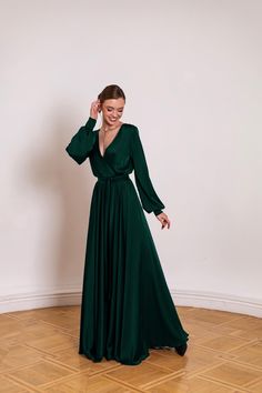 a woman in a long green dress standing on the floor with her hands behind her head