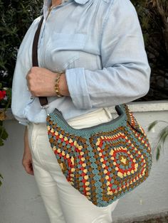 a woman holding a crocheted purse in her right hand while wearing white pants and a blue shirt