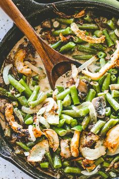 a skillet filled with green beans and shrimp next to a wooden spoon on top of a table