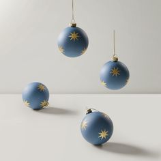 three blue christmas balls with gold stars hanging from the top, on a white surface