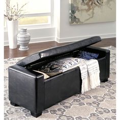 a black leather storage bench with pillows and blankets on it in a living room area