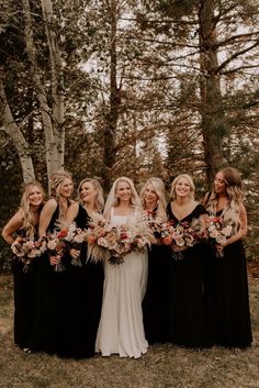 a group of women standing next to each other holding bouquets in front of trees