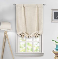 a window with a curtain hanging on the side of it and a lamp next to it