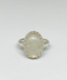 This cool, white Rainbow Moonstone gemstone ring reminds me of the puffy clouds that accent a Spring day. After a rain you can see the dark clouds turn to wisps of white with a faint rainbow glistening through. This stone is just that! As you look at the ring and turn it you will see subtle flashes of blue purple and maybe green. The lovely way the stone is nestled within the Sterling silver scalloped bezel setting gives this special piece a dainty yet bold look and feel. Designed in a timeless Celestial White Moonstone Birthstone Ring, Celestial White Moonstone Ring As Birthstone, Celestial Style White Moonstone Birthstone Ring, Celestial White Promise Ring Jewelry, White Celestial Jewelry For Promise Ring, Celestial White Moonstone Ring With Halo, Celestial Style White Moonstone Ring With Halo, White Moon-shaped Birthstone Rings, White Moon Shaped Ring With Birthstone