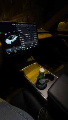 a car dashboard with a monitor and bottles on the table in front of it at night