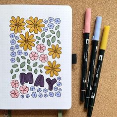 an open notebook with flowers and the word may written in large letters on it next to markers