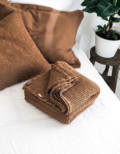 a bed topped with pillows and blankets next to a potted plant