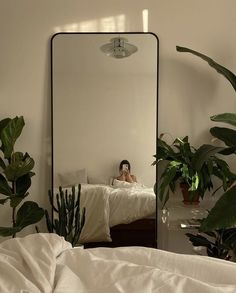 a mirror reflecting a woman sitting on a bed in front of a potted plant