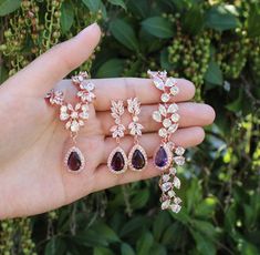 a person is holding three pairs of earrings in their hand, one with purple stones and the other with white diamonds