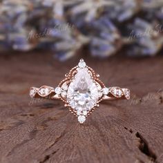 an engagement ring with a pear shaped cut diamond in the center, on top of a piece of wood