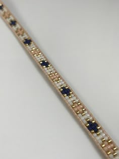 a gold and white bracelet with blue beads on it's end, sitting on a table