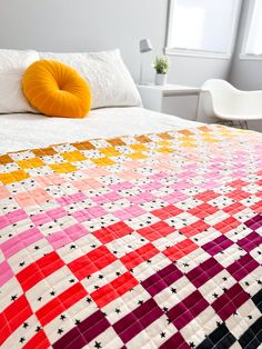 a bed with a colorful quilt on top of it next to a white chair and window