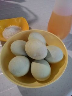 a yellow bowl filled with white eggs next to a glass of orange juice and spoon